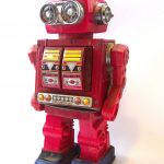Red children’s toy robot. Has silver eyes, a panel on the torso and blue feet.