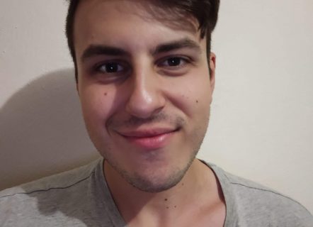 Close-up photo of a dark haired man wearing a grey t-shirt and smiling at the camera