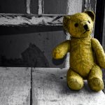 Old yellow teddy bear on an old flaking white wooden chair.