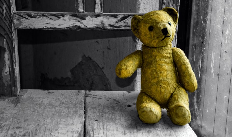Old yellow teddy bear on an old flaking white wooden chair.