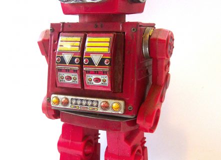 Red children’s toy robot. Has silver eyes, a panel on the torso and blue feet.